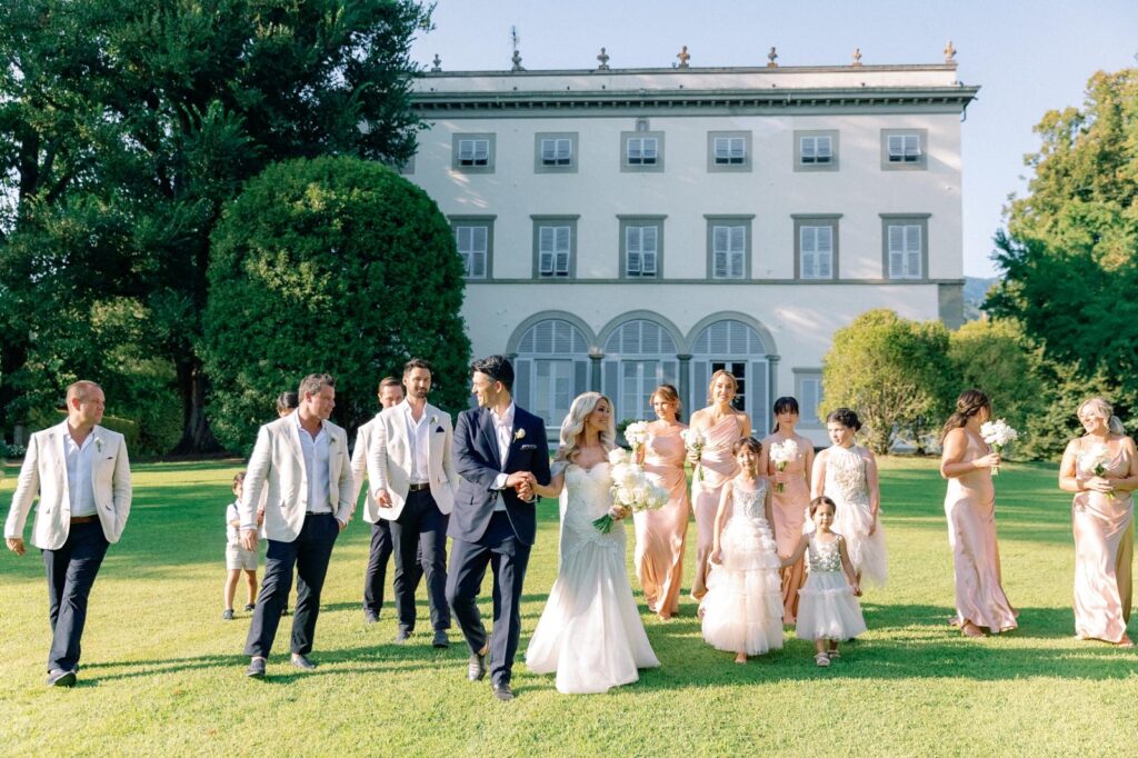 Bride and groom walking across the gardens with their bridal party outside an elegant European-style wedding estate, celebrating after their ceremony.